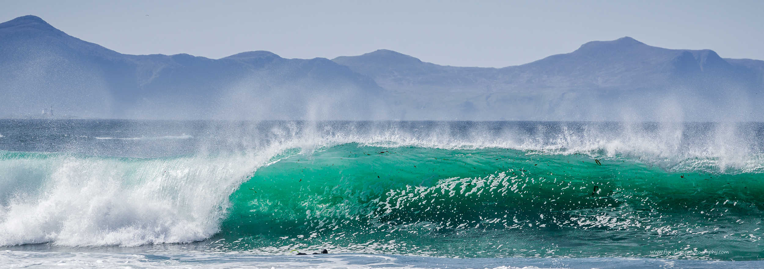 Surfer padler ut mot stor bølge.