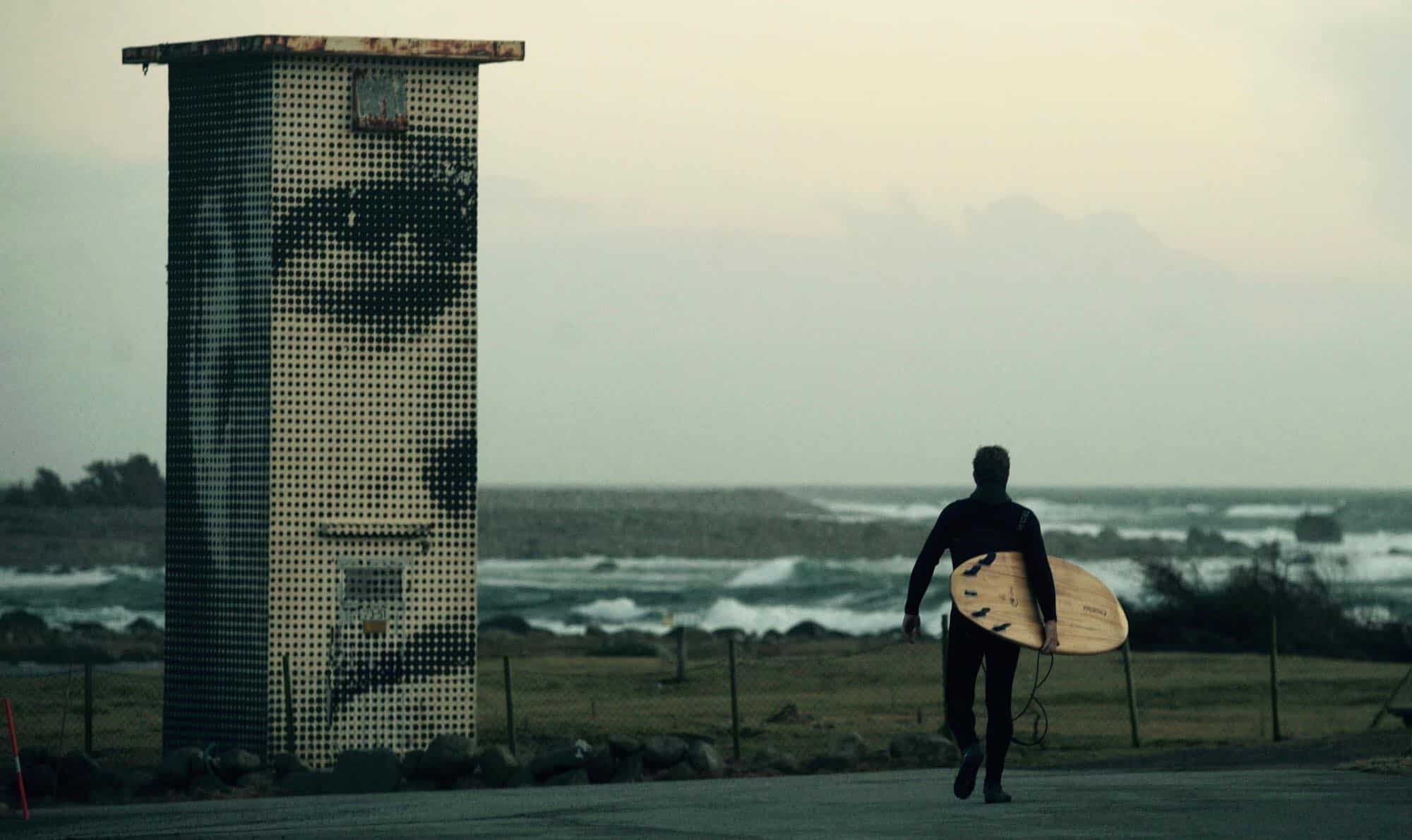 Surfer går forbi kunstverk på Lista
