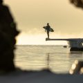 Surfer står på frossen brygge og ser utover havet.